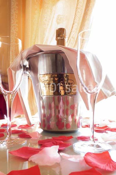 Seau à champagne avec bouteille et deux flûtes sur une table décorée de pétales de rose, devant un rideau doré.