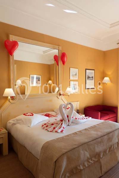 Lit décoré avec des serviettes en forme de cygnes et des pétales rouges, dans une chambre aux tons chauds avec des ballons…