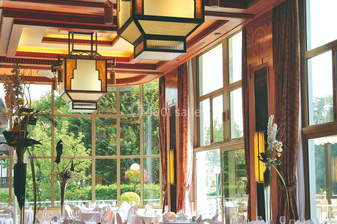 Salle de restaurant élégante avec grandes baies vitrées, tables dressées et luminaires suspendus au plafond.