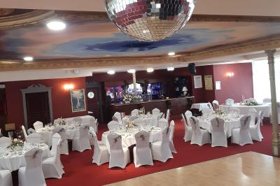 Salle de réception avec scène, piste de danse en bois, moquette rouge et plafond décoré d'une fresque.