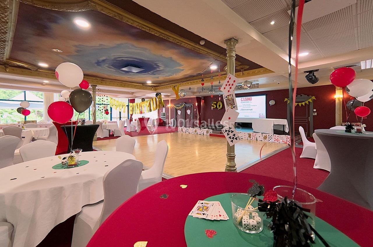 Salle décorée sur le thème du casino avec tables blanches, ballons, cartes à jouer et piste de danse au centre.