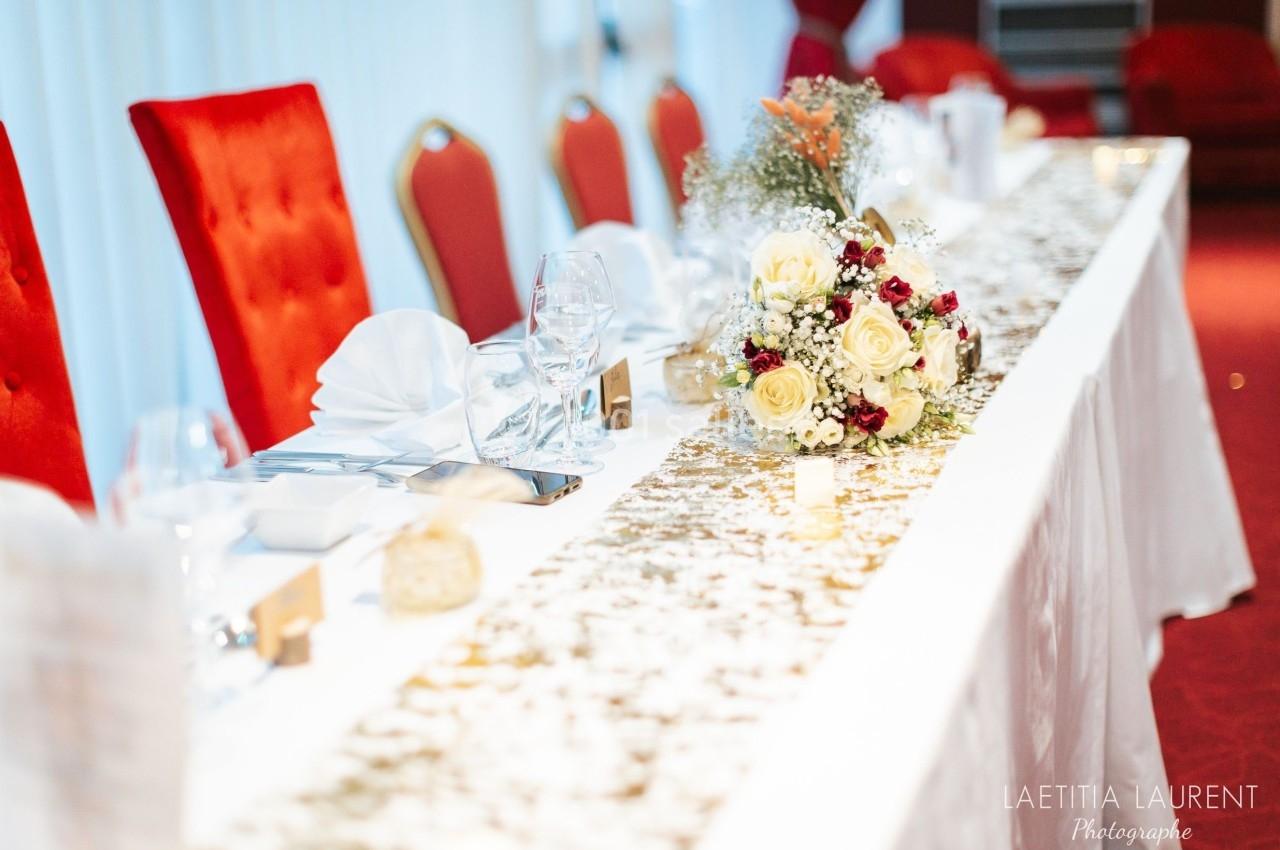 Table de réception élégamment dressée avec nappes blanches, vaisselle raffinée et bouquet floral au centre.