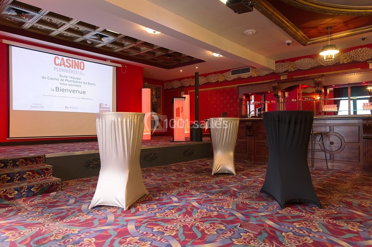 Salle de réception avec tables hautes drapées, écran de projection allumé et décorations de style classique.