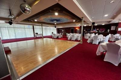 Salle de réception avec scène, piste de danse en bois, moquette rouge et plafond décoré d'une fresque.