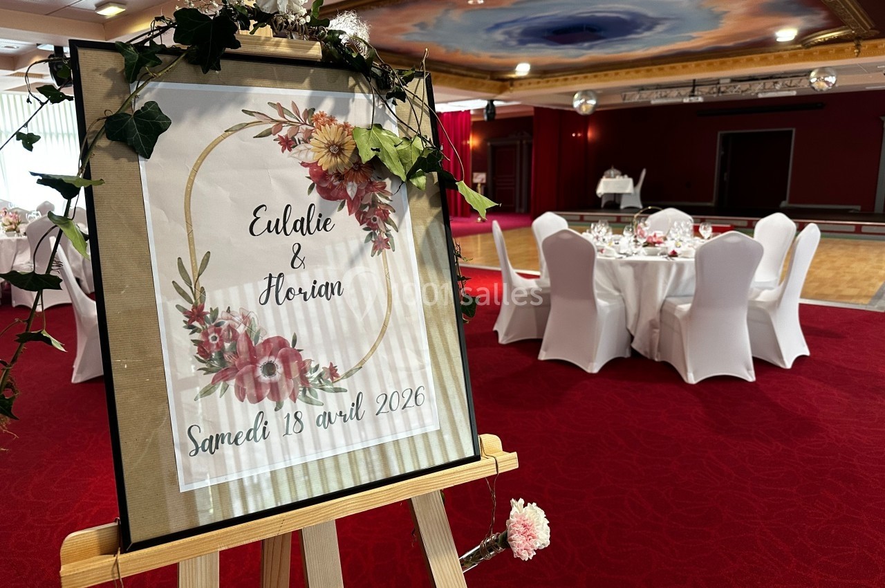 Panneau décoratif annonçant un mariage avec des fleurs, posé sur un chevalet dans une salle de réception.