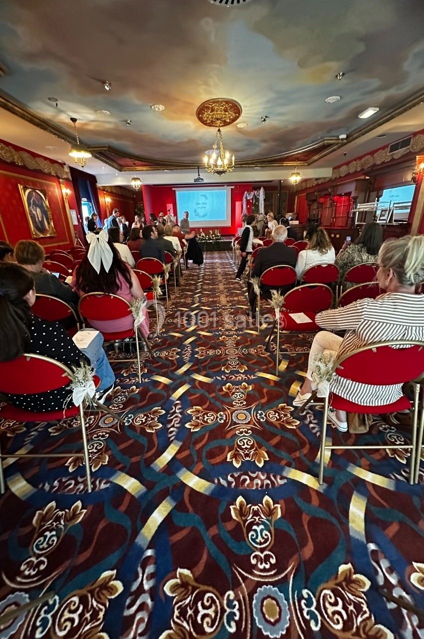 Personnes assises dans une salle ornée de décorations rouges et dorées, assistant à une présentation sur écran.
