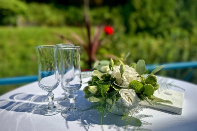 Deux verres à pied et un bouquet de fleurs blanches et vertes sur une table ronde en extérieur.