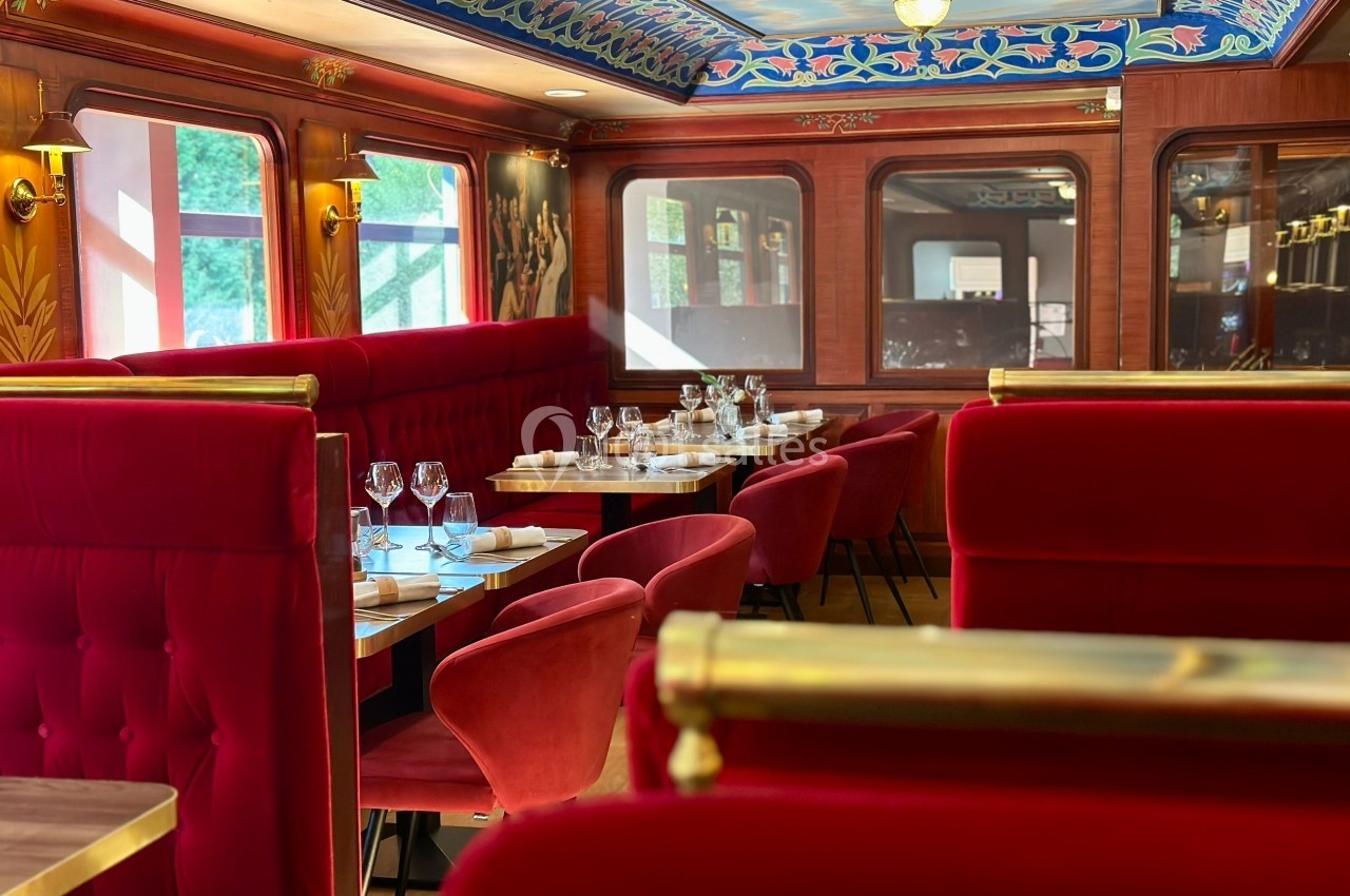 Intérieur d'un wagon-restaurant élégant avec banquettes rouges, tables dressées et décorations raffinées.