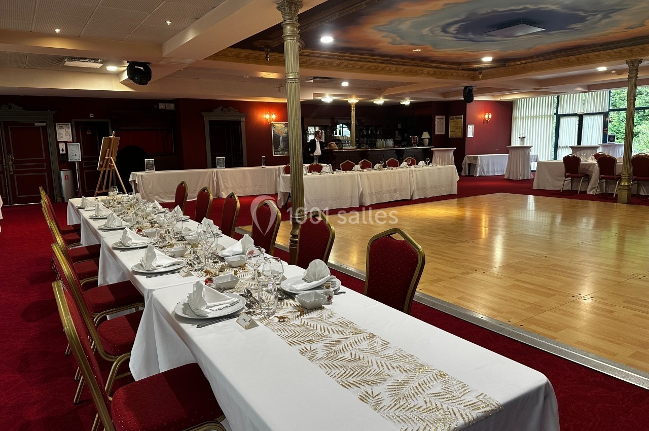 Disposition autour de la piste Salle de réception avec tables dressées, chaises rouges, piste de danse en bois et bar en arrière-plan.
