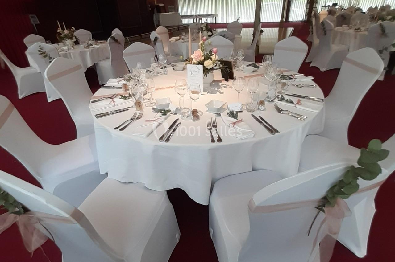 Disposition idéale pour un mariage Table ronde élégamment dressée avec nappes blanches, couverts, verres, bougies et centre de table floral.