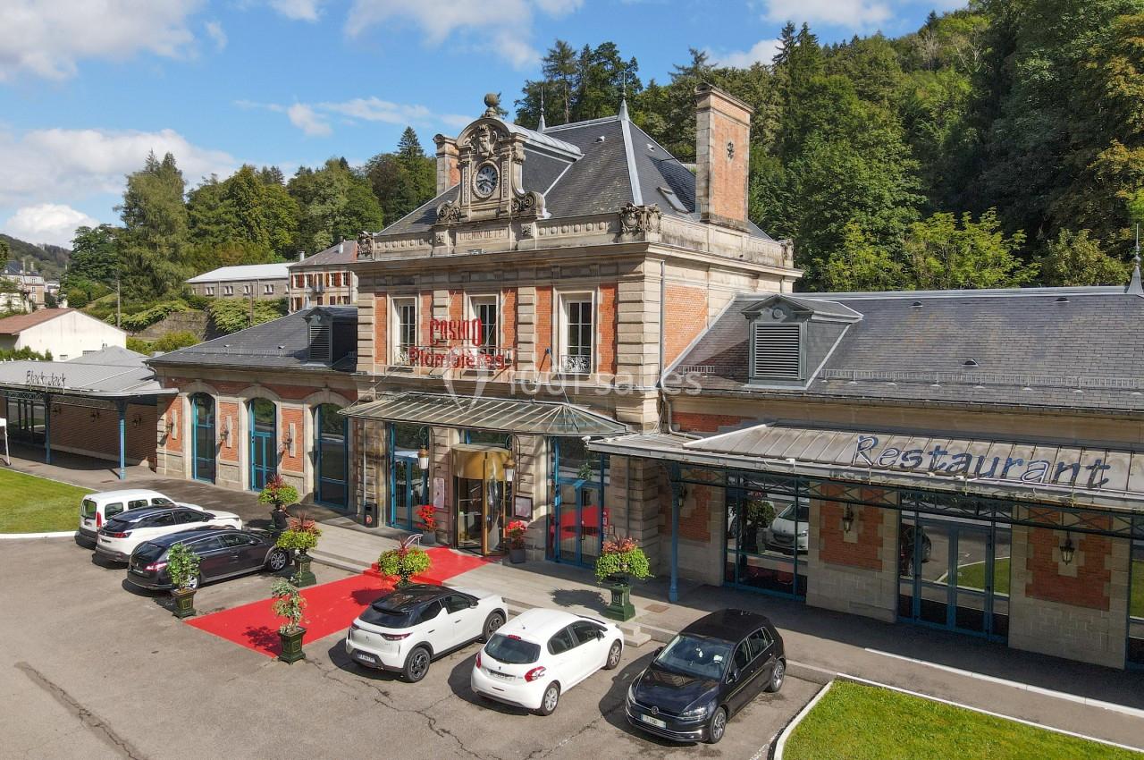 Façade d'un bâtiment historique avec une entrée principale, des voitures garées et un auvent marqué ’Restaurant’.