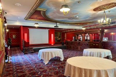Salle de réception avec scène, piste de danse en bois, moquette rouge et plafond décoré d'une fresque.