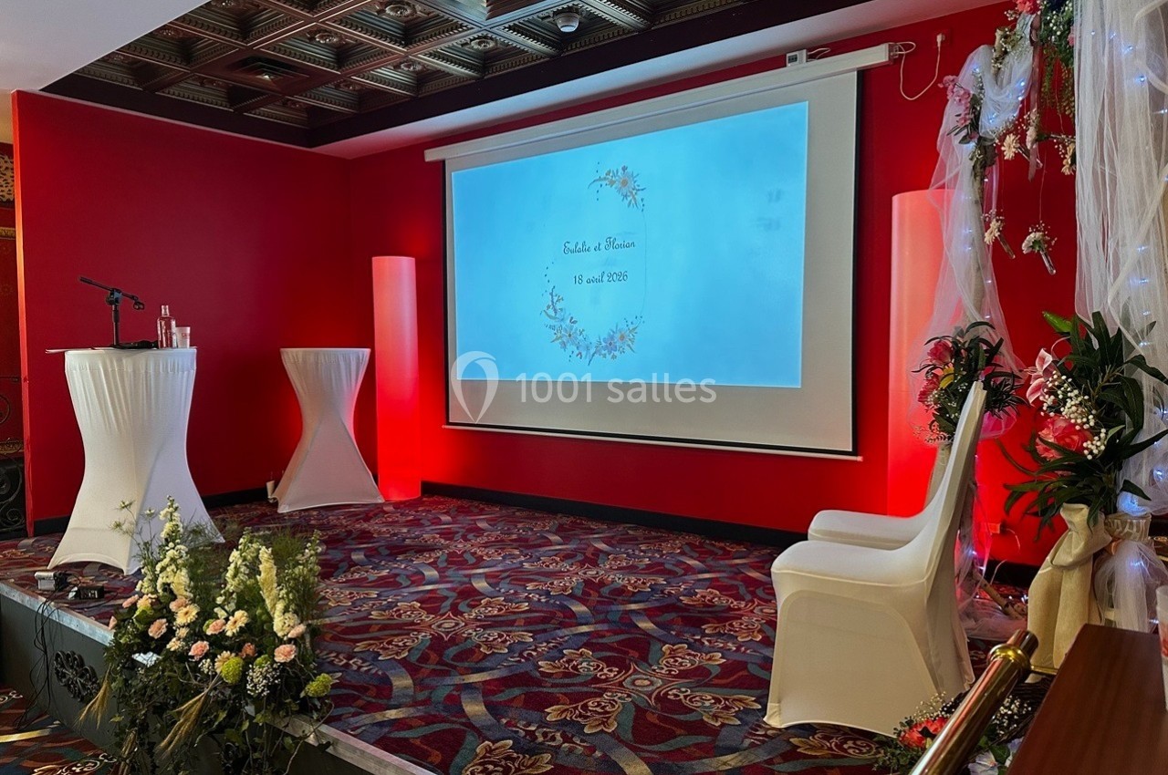 Salle décorée pour un mariage avec écran projetant les prénoms des mariés, fleurs et chaises blanches.