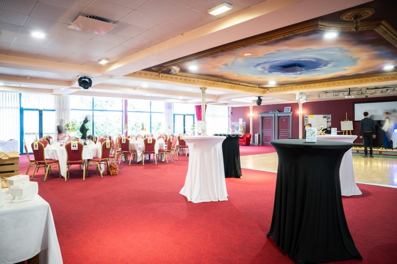 Salle privatisée pour un anniversaire Salle de réception avec tables dressées, nappes blanches, chaises rouges et piste de danse sous un plafond décoré.