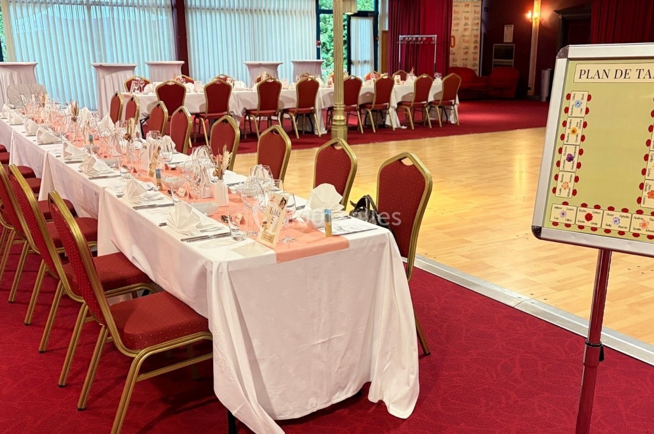 Salon Impérial à l'occasion d'un baptême Salle de réception avec tables dressées, chaises rouges et un plan de table affiché près d'une piste de danse.