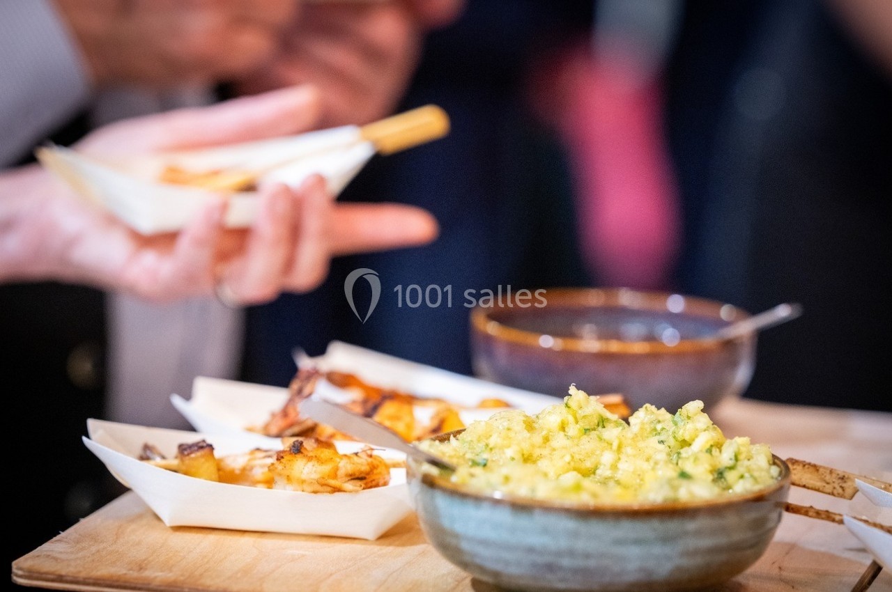 Des plats de nourriture, dont des brochettes et une salade, sont disposés sur une table en bois lors d'un événement.