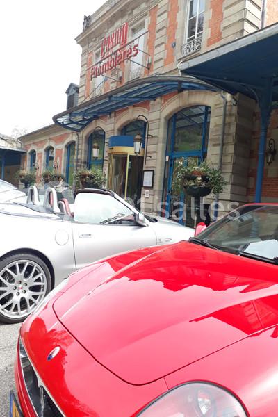 Accès et parking facilités aux abords de l'établissement Deux voitures décapotables garées devant un bâtiment en briques avec une enseigne ’Casino Plombières’.