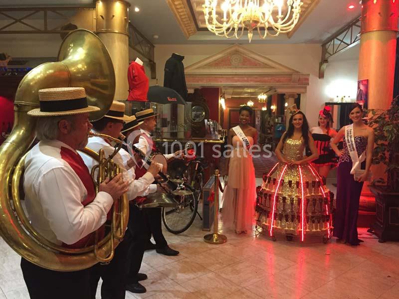 Accueil en fanfare Un groupe de musiciens joue devant quatre femmes en robes élégantes dans un hall éclairé.