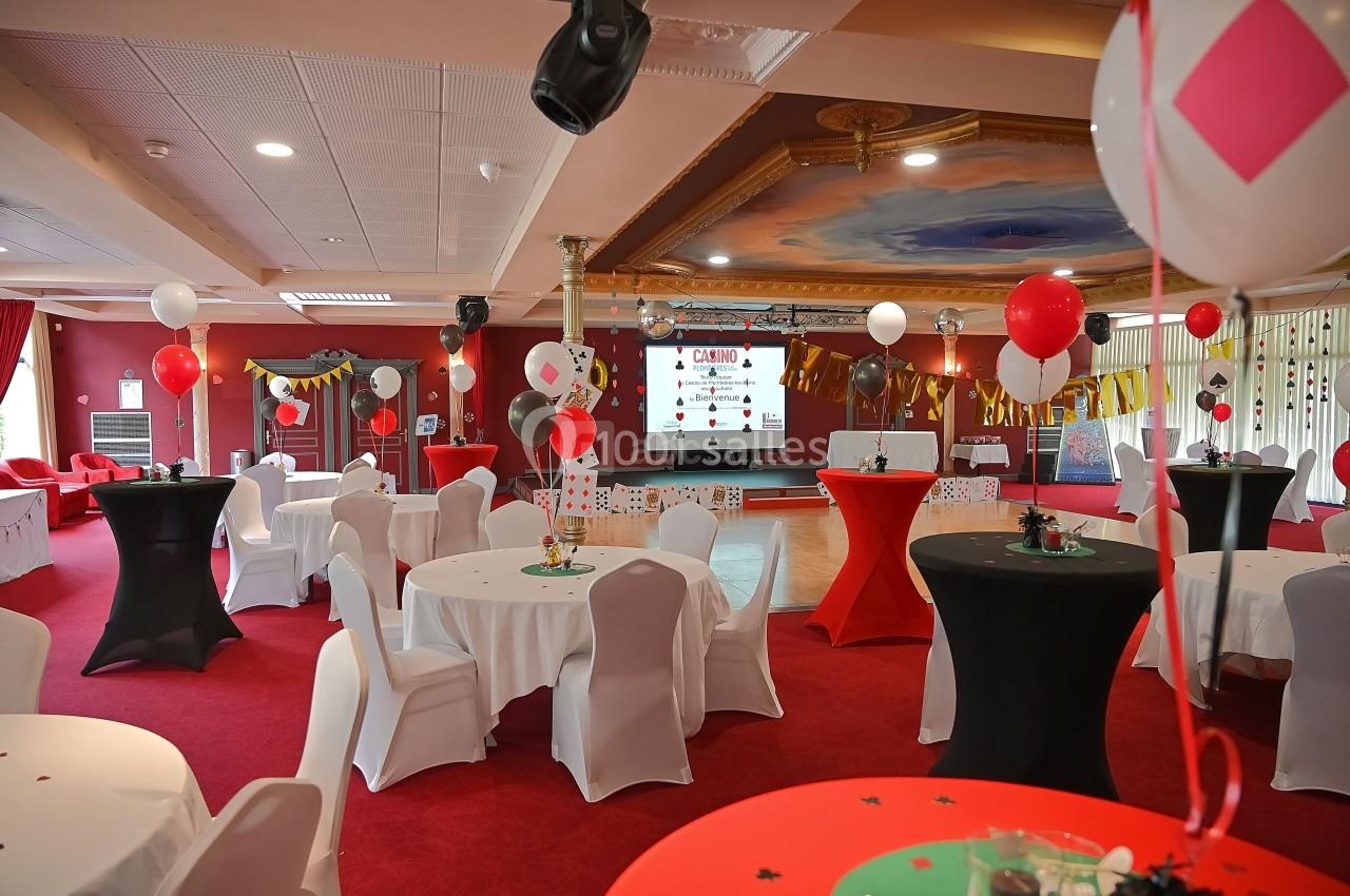Ambiance anniversaire surprise au Salon Impérial Salle décorée sur le thème du casino avec tables rondes, nappes blanches, ballons et écran de projection.