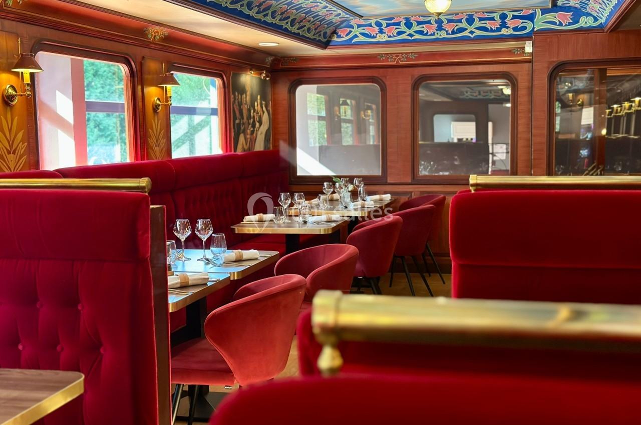 Ambiance feutrée et raffinée dans le wagon Salle de restaurant élégante avec banquettes rouges, tables dressées et décorations murales raffinées.