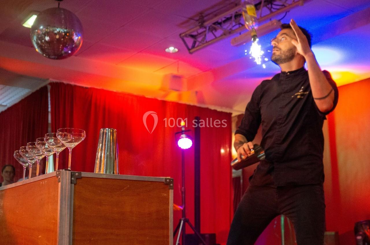 Animation Show Flair pour créer l'évènement Un barman réalise un spectacle de flair bartending avec des verres et un shaker dans une salle éclairée.