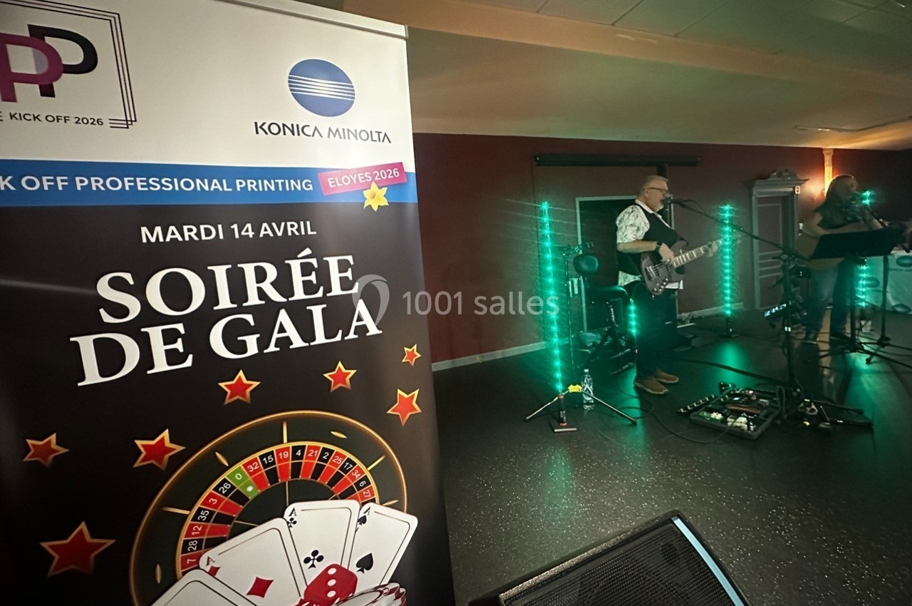 Un musicien joue de la guitare sur scène lors d'une soirée de gala, avec une affiche promotionnelle au premier plan.