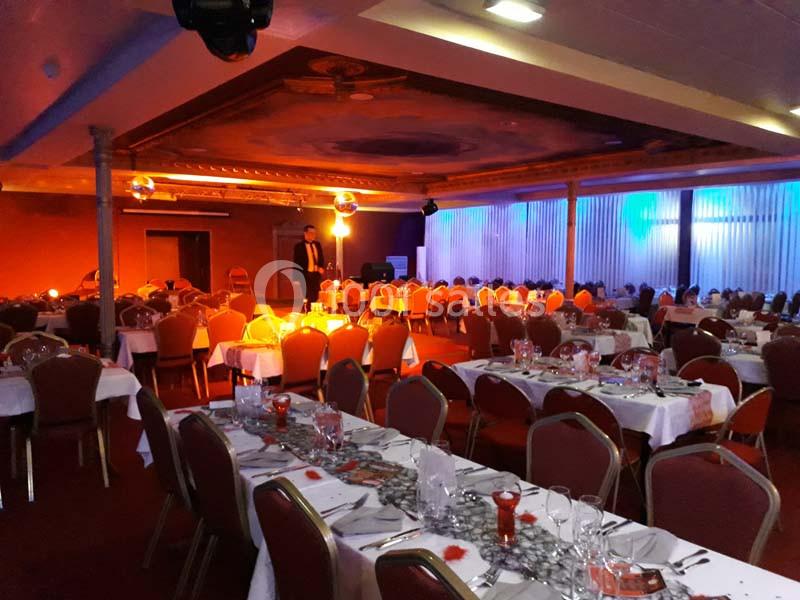 Avant l'arrivée des invités Salle de réception décorée avec des tables dressées pour un événement, éclairage chaleureux et ambiance festive.