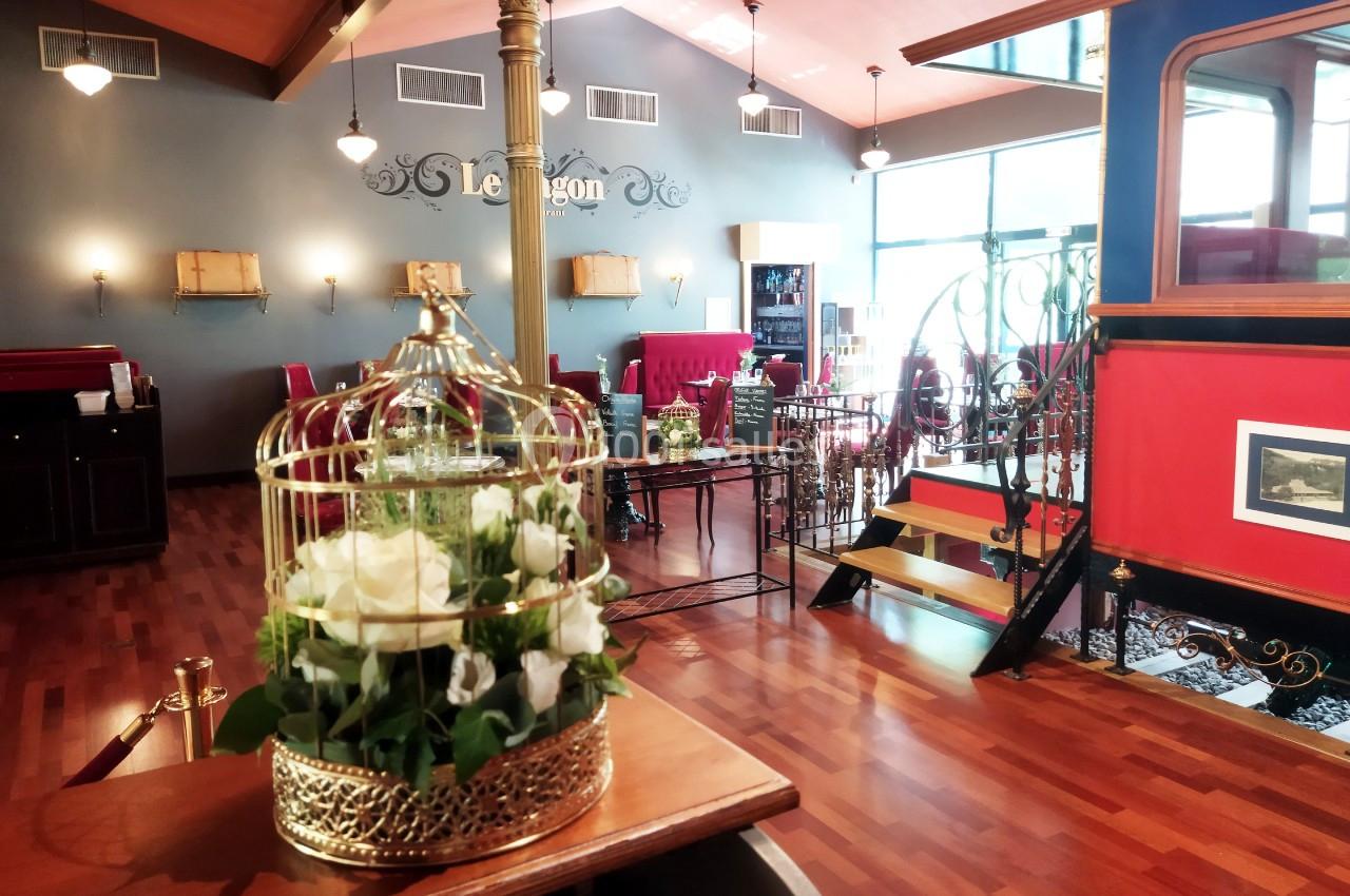 Bienvenue au Restaurant Le Wagon Salle de restaurant élégante avec parquet, mobilier rouge, escalier en fer forgé et fleurs blanches en cage dorée.
