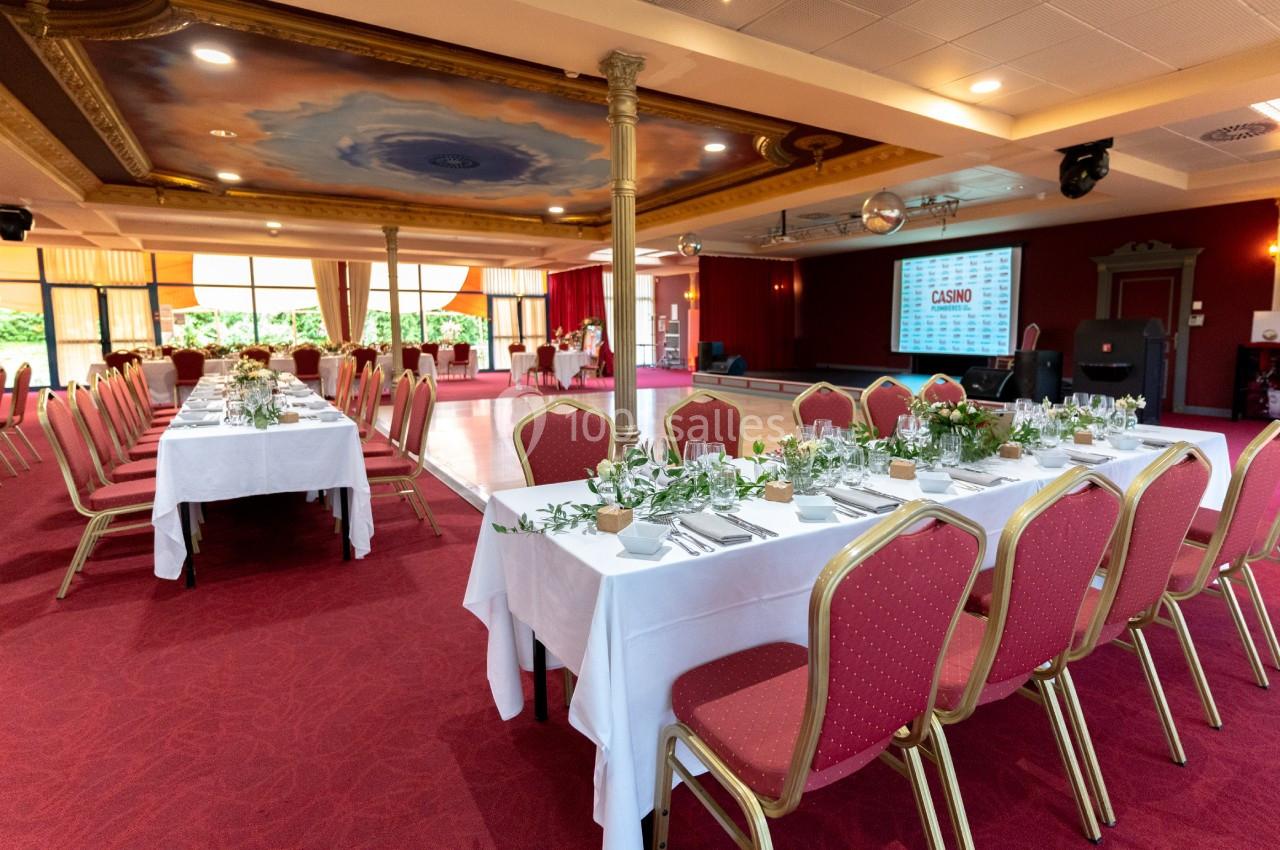 En mode dîner de gala Salle de réception avec tables dressées, nappes blanches, chaises rouges et décoration végétale, prête pour un événement.