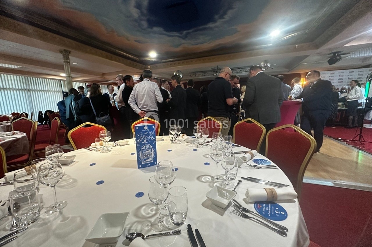 Salle de réception avec des tables dressées au premier plan et un groupe de personnes debout en discussion à l'arrière-plan.
