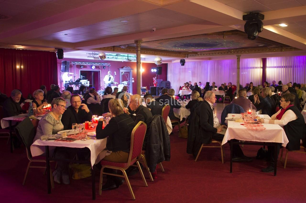 Haut lieu du spectacle et des dîners dansants Salle de réception avec des convives assis à des tables, éclairée par des lumières tamisées et une scène en arrière-plan.
