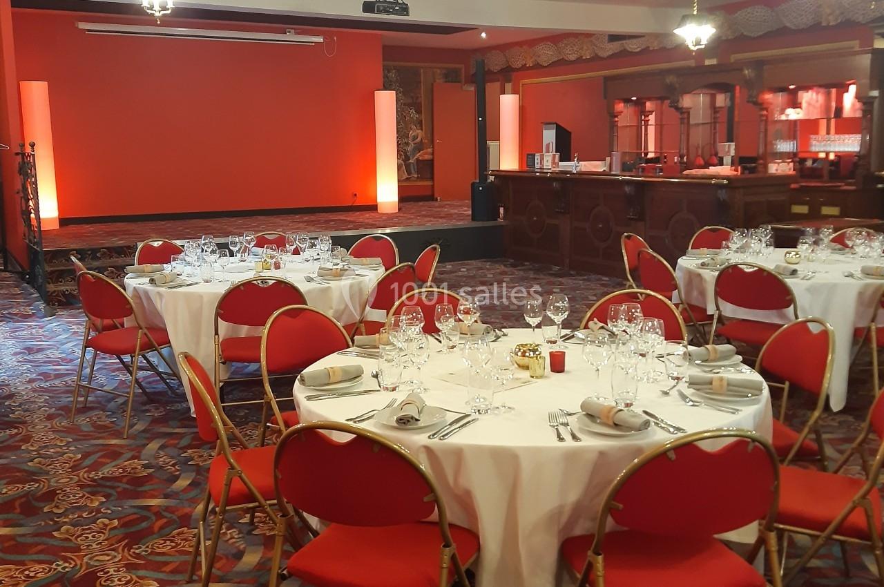 Juste avant une soirée animée Salle de réception avec tables rondes dressées, chaises rouges et éclairage chaleureux.