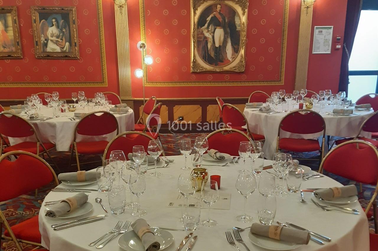 L'Empereur veille sur vos convives Salle de réception élégante avec tables rondes dressées, nappes blanches, chaises rouges et décorations murales classiques.