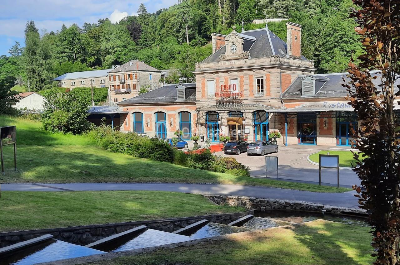 Le Casino face au parc impérial Bâtiment en briques rouges avec horloge, entouré de verdure, situé près d'un ruisseau et d'une pente herbeuse.