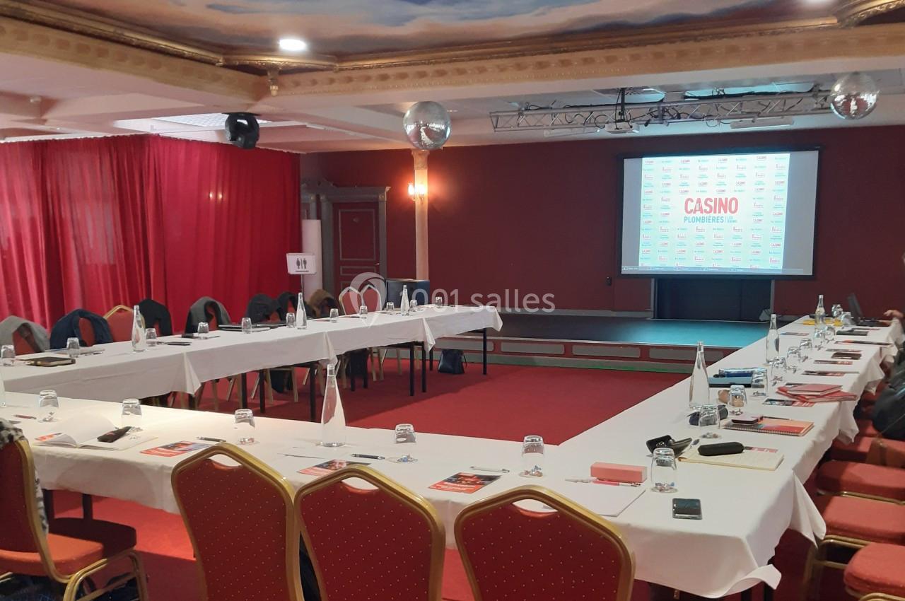 Le Salon Impérial est adapté à toutes les configurations Salle de réunion avec tables disposées en U, chaises rouges, écran de projection et rideaux rouges en arrière-plan.