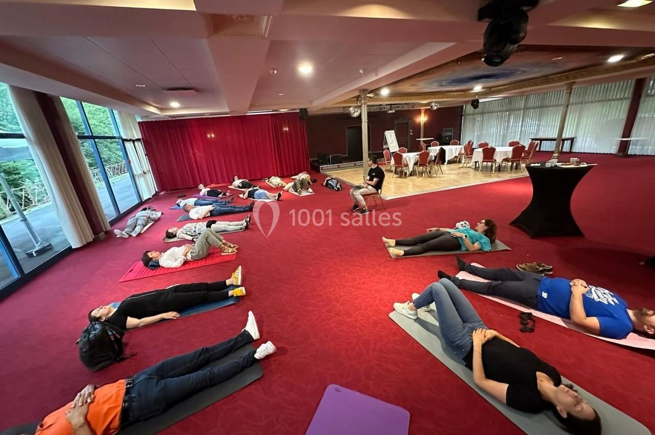 Pour vos activités de détente : team building apaisant Personnes allongées sur des tapis dans une salle avec moquette rouge, participant à une séance de relaxation ou de…