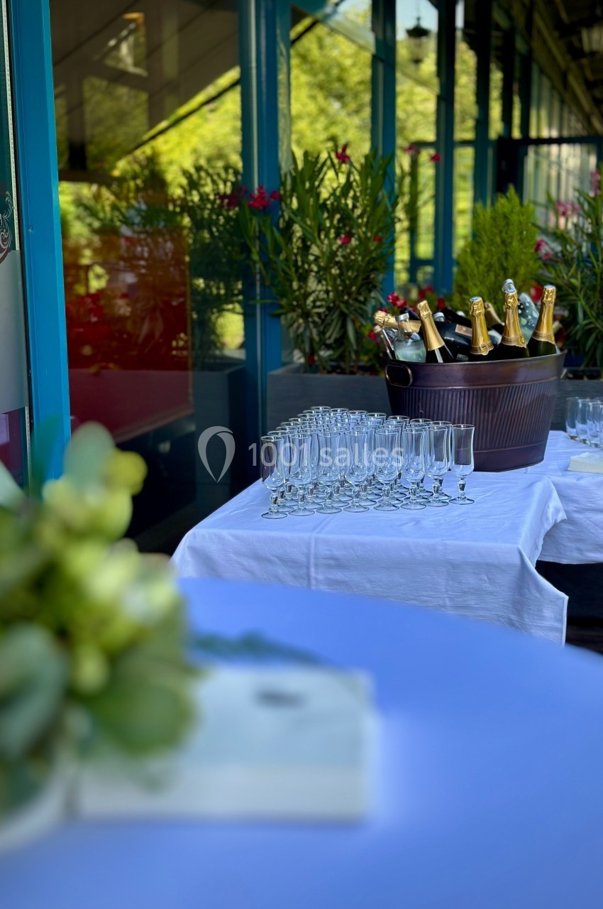 Seau rempli de bouteilles de champagne avec des flûtes alignées sur une table blanche en extérieur.