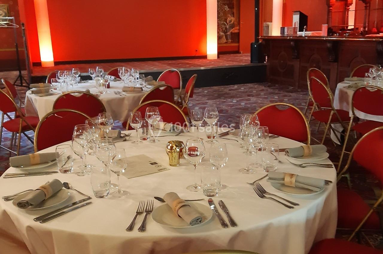 Repas et réception au Salon de l'Empereur Salle de réception avec tables rondes dressées, nappes blanches, chaises rouges et éclairage mural orange.