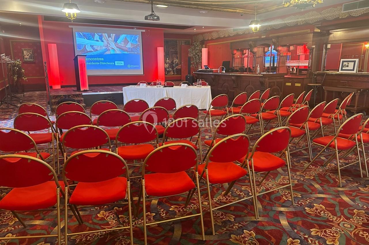 Réunion ou conférence au Salon de l'Empereur Salle de conférence avec rangées de chaises rouges, écran de présentation allumé et table blanche à l'avant.