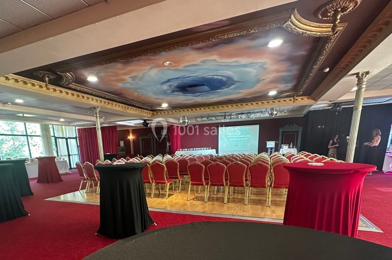 Salle de réception avec plafond peint, chaises alignées face à un écran de projection, tables hautes en premier plan.