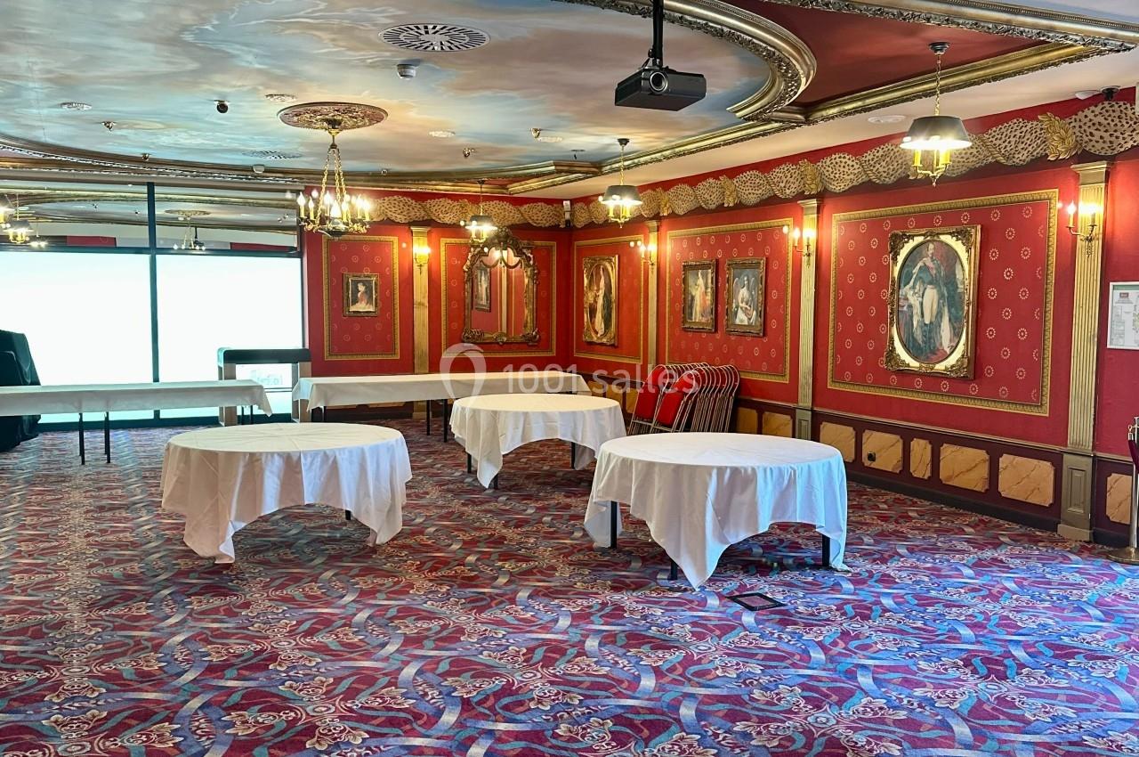 Salon de l'Empereur proposé avec ou sans mobilier Salle décorée de rouge avec tapis à motifs, tables recouvertes de nappes blanches et cadres accrochés aux murs.