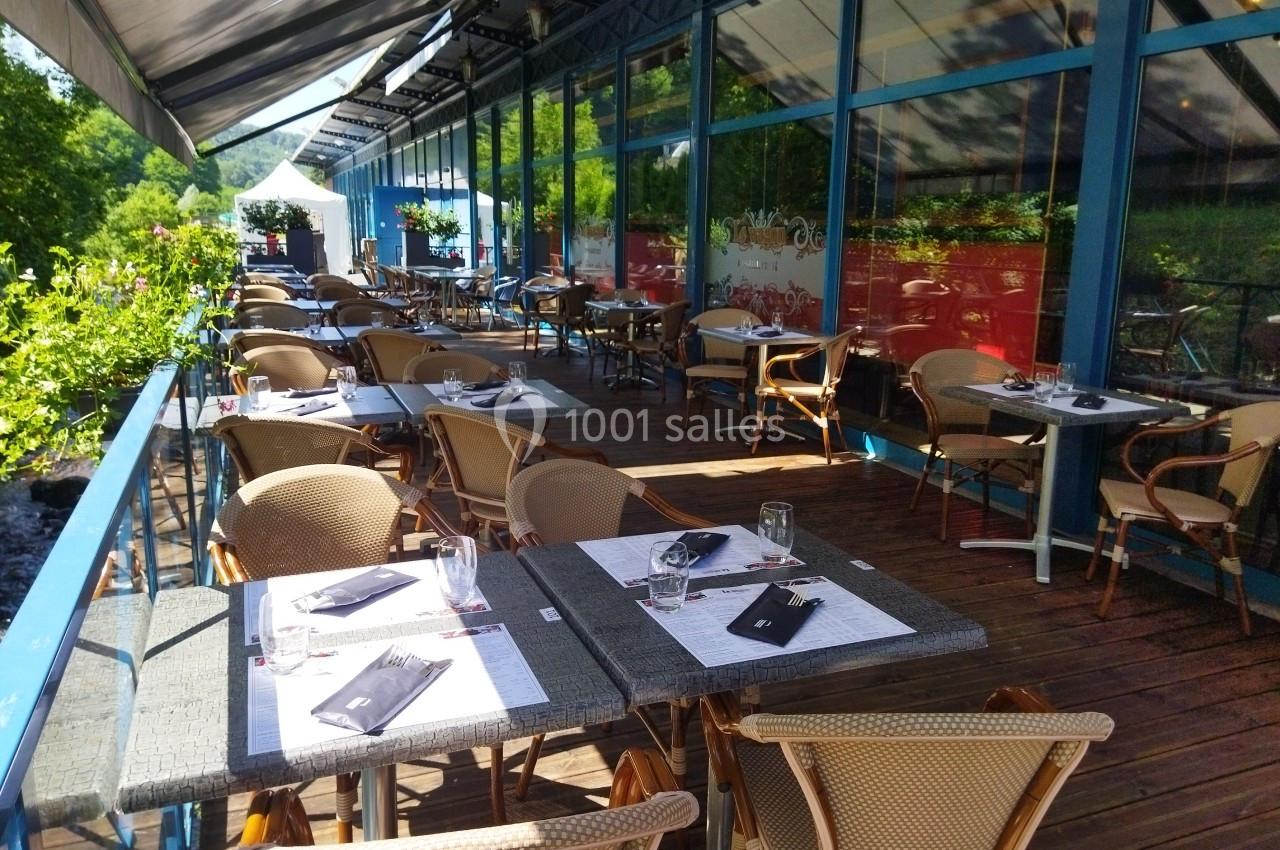 Terrasse du Restaurant, privatisable Terrasse ensoleillée d'un restaurant avec des tables dressées, entourée de verdure et bordée par un cours d'eau.