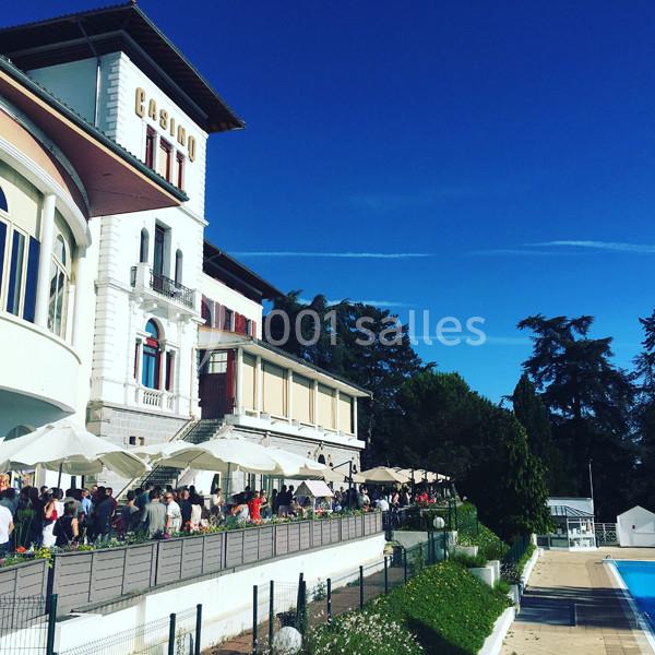 Location salle Saint-Galmier (Loire) - Casino de Saint-Galmier #14 Façade d'un bâtiment avec l'inscription ’Casino’, terrasse animée, parasols blancs et piscine en contrebas.