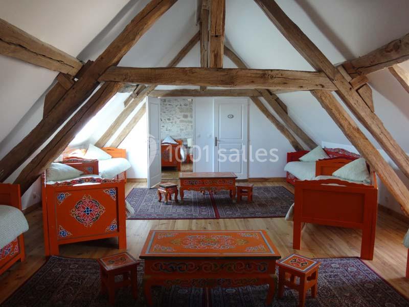 Chambre mansardée avec poutres apparentes, meubles en bois peint orange et tapis sur un sol en parquet.