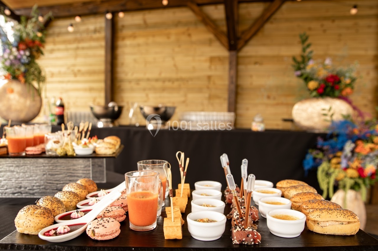 Buffet avec verrines, macarons, brochettes et pains disposés sur une table en bois dans un cadre extérieur décoré.