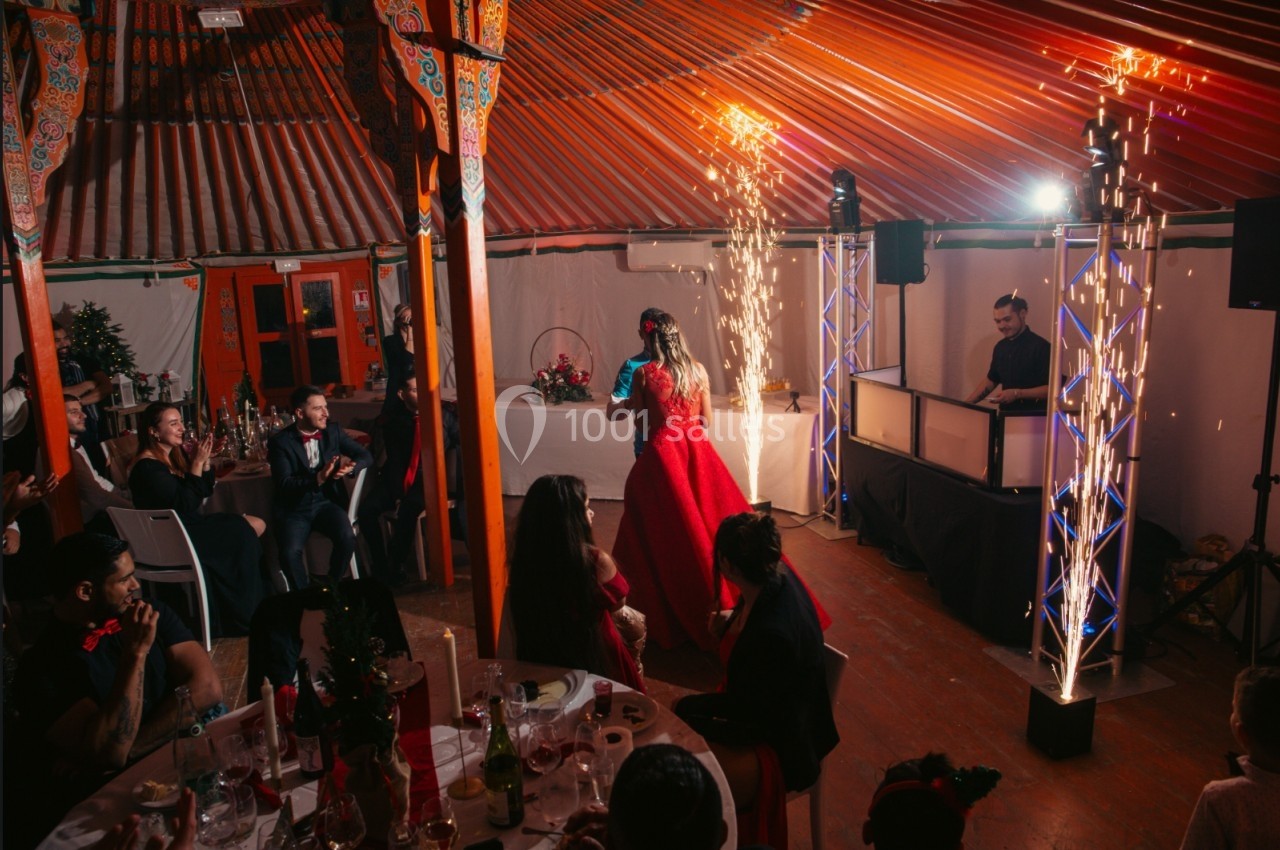 Une femme en robe rouge danse sous des étincelles dans une salle décorée, entourée d'invités assis.