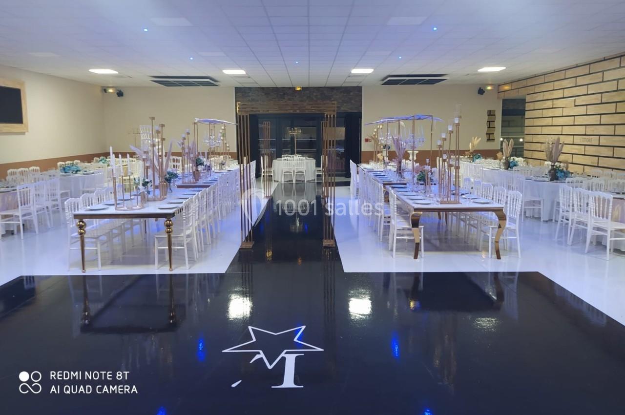 Salle de réception décorée avec des tables alignées, des chaises blanches et une piste noire centrale ornée d'une étoile.