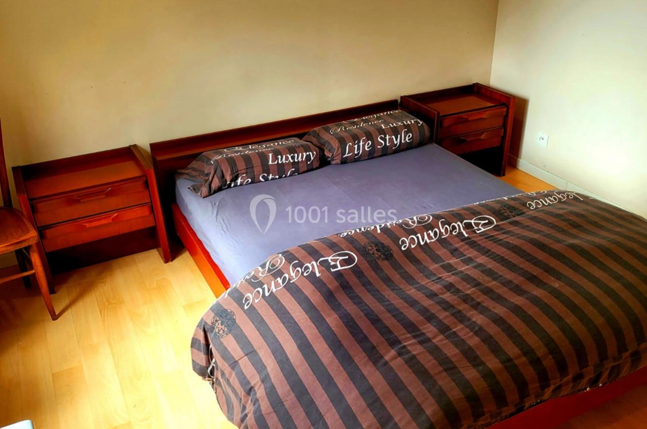 Lit double avec draps marron à motifs, encadré par deux tables de chevet en bois dans une chambre lumineuse.