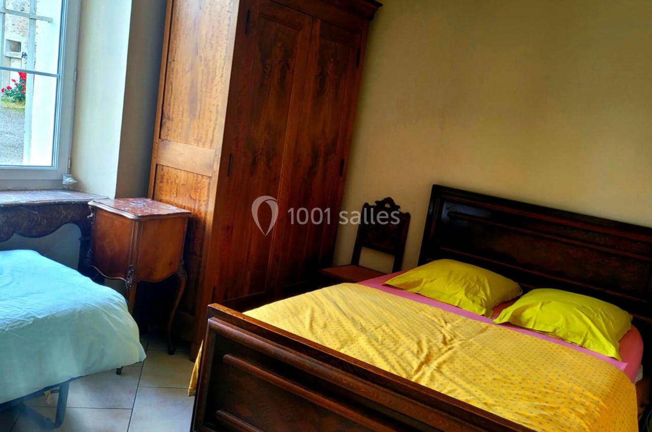 Chambre avec lit double en bois, armoire ancienne, table de chevet et lit simple près d'une fenêtre.
