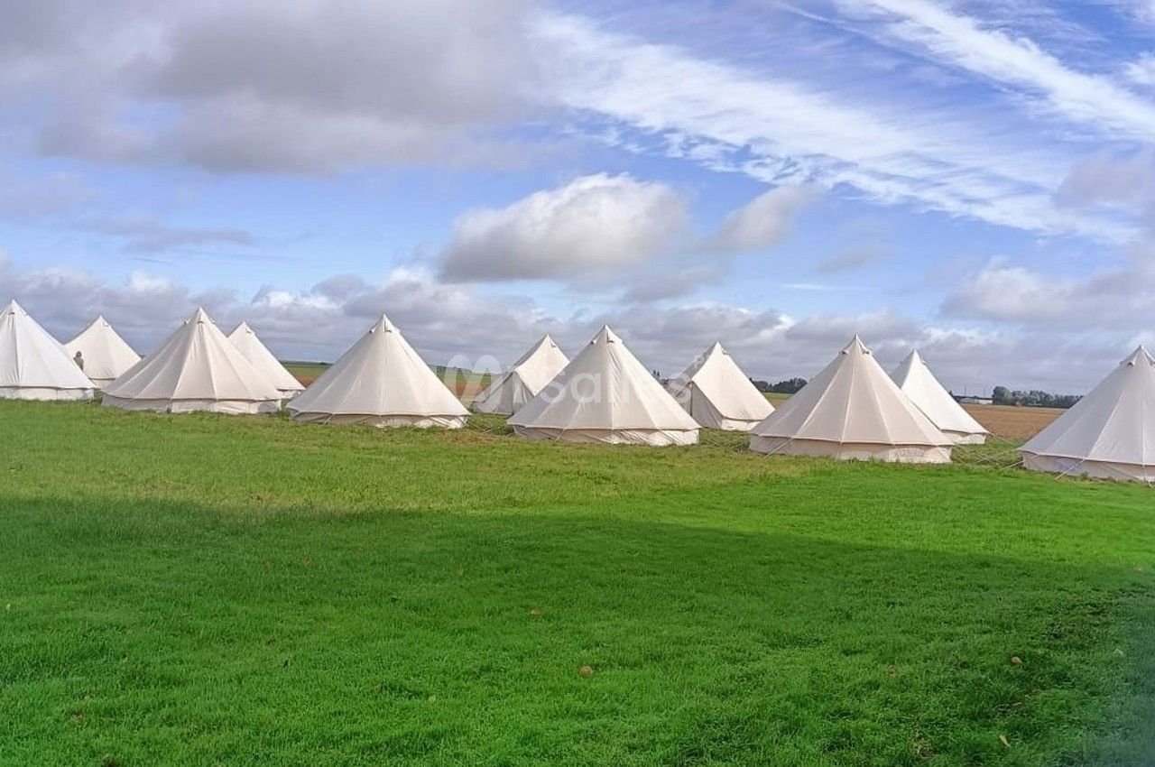 Tentes blanches en toile disposées sur une prairie verte sous un ciel partiellement nuageux.